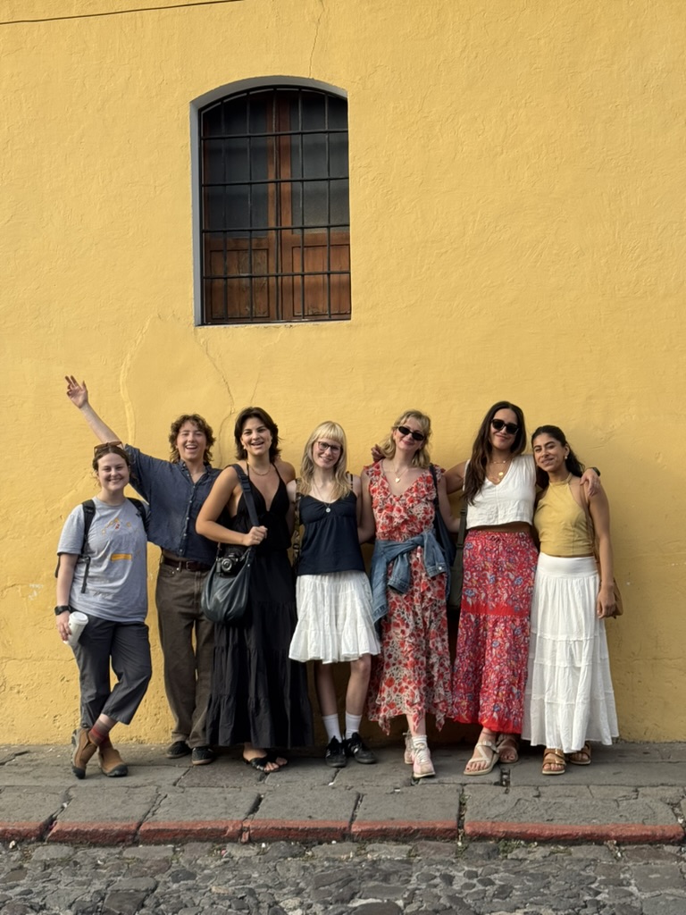 Seven friends standing against a yellow wall